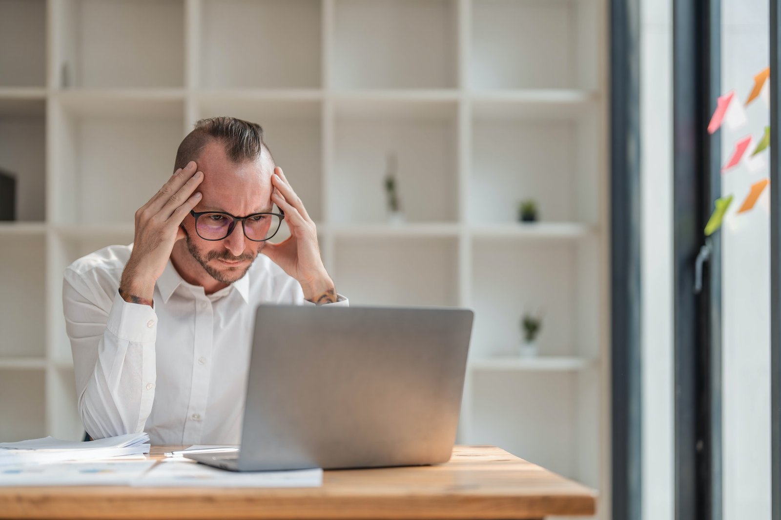 Young unhappy man office worker feeling bored at work, looking at laptop with demotivated face